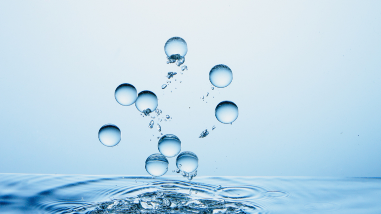 Blue-tinted water with bubbles rising from a splash on the surface across a calm pool.