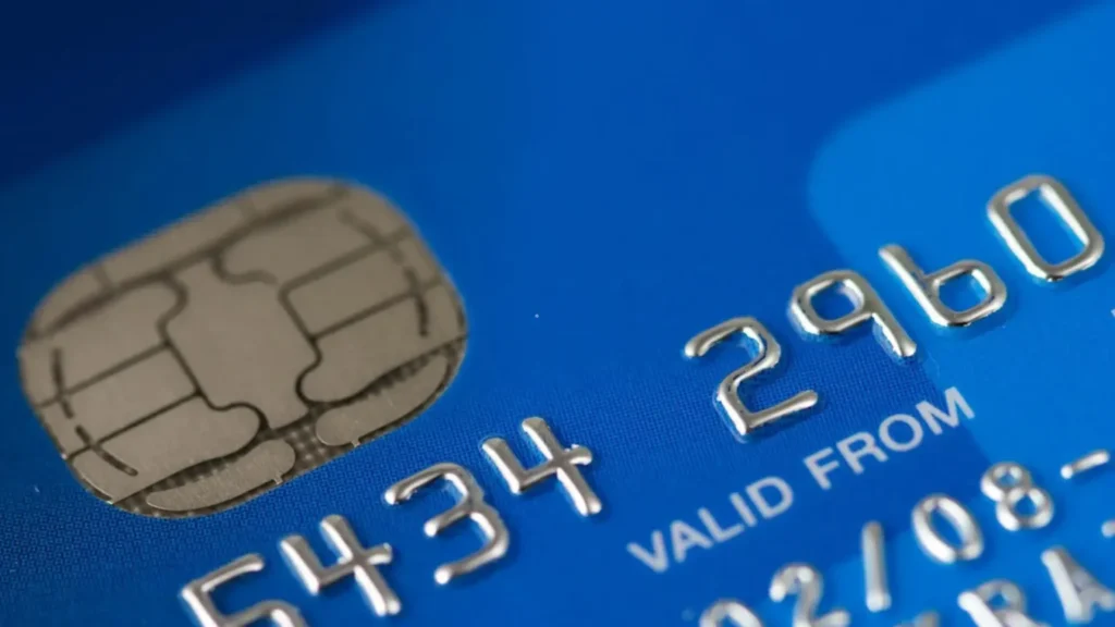 Close-up of a blue credit card showing a silver EMV chip and embossed digits, with 'VALID FROM' text visible.
