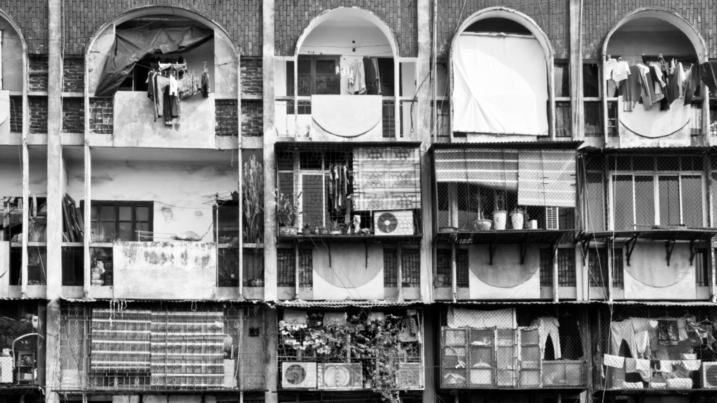 Row of aged apartment balconies with laundry hanging and arched openings, in black and white.
