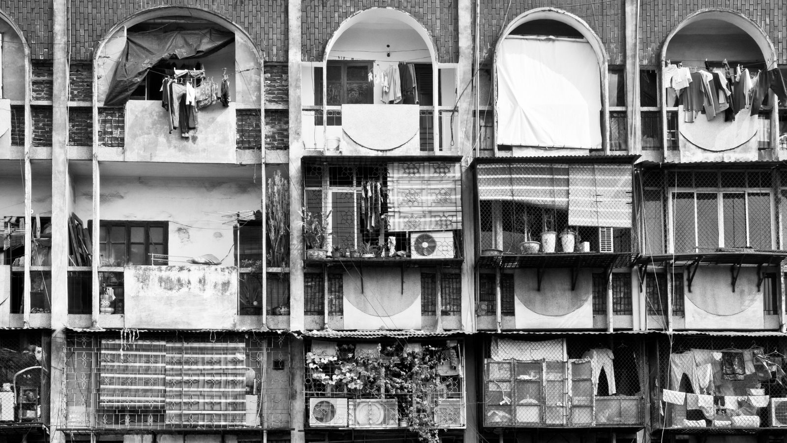 Row of aged apartment balconies with laundry hanging and arched openings, in black and white.